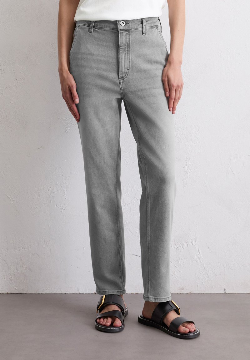 Pantalons en denim gris à coupe droite, design à cinq poches et fermeture à bouton. Portés avec des sandales noires ornées d'un accent doré.