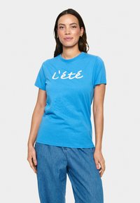 T-shirt en coton bleu avec des manches courtes et un col rond, comportant le texte "l'été" en police cursive blanche sur le devant.