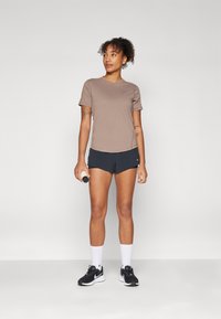 Kort brun atletisk T-skjorte, svarte shorts og svarte joggesko. Fremtredende trekk inkluderer korte ermer, logo på skjorten og hvite sokker.