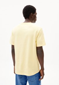 Gelbes Baumwoll-T-Shirt mit Rundhalsausschnitt, kurzen Ärmeln und lockerer Passform. Die Rückansicht zeigt eine glatte, einfarbige Textur und einen geraden Saum.