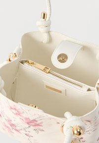Bolso blanco con diseño floral rosa, cremallera dorada, cierre magnético y asas de cordón anudado. Bolsillo interior con cremallera visible.