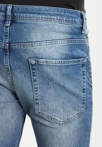 Bleka blå denimjeans med en bakficka med en dekorativ sydd kontur, rak skärning och en något texturerad yta.