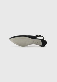 Scarpa slingback nera in suede con punta affusolata, tacco sottile e cinturino con fibbia. Sole grigio strutturato con scanalature per una migliore aderenza.