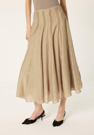 Jupe midi beige de coupe trapèze avec des détails de coutures verticales, portée avec des chaussures slingback noires à talon kitten.