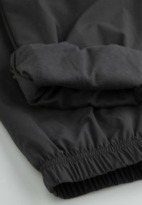 Czarny elastyczny materiał o gładkiej fakturze, z elastycznym pasem. Materiał jest złożony, ukazując jego grubość i miękkość.