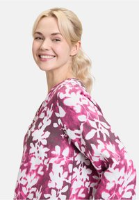 Bluse mit floralem Muster in Rosa- und Weißtönen, mit einem lockeren Schnitt, V-Ausschnitt und langen Ärmeln. Weicher Stoff mit leichter Textur.
