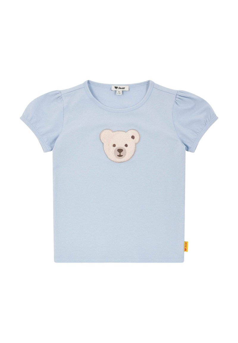 Camiseta azul claro con mangas cortas abullonadas, que presenta un aplique de oso en beige y marrón en el centro y una etiqueta amarilla en el lateral.
