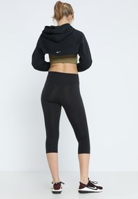 Felpa nera corta con cappuccio, abbinata a un reggiseno sportivo verde oliva, leggings neri e scarpe da ginnastica scure. Materiali lisci e aderenti.