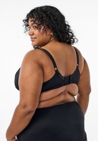Reggiseno nero con spalline regolabili, tessuto texturizzato e chiusura a gancio e asola sul retro. Presenta bordi lisci e dettagli rotondi.