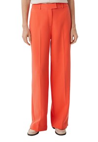 Jasnopomarańczowe, szerokie spodnie wykonane z gładkiego materiału, z plisami z przodu, ze wstążką w talii i dopasowanym krojem. Podkreślone czystym wzornictwem.