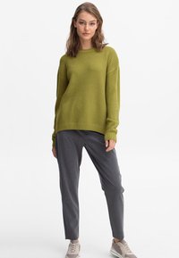 Groene textuur trui met geribbelde manchetten en zoom, gecombineerd met grijze tapered broek en lichtgrijze sneakers. Eenvoudige en ontspannen pasvorm.
