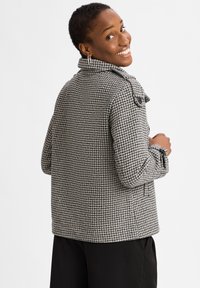 Black and white houndstooth-patterned jacket with a collar, side pockets, and button accents, made of textured fabric.
