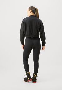Svart cropped sweatshirt, tettsittende svarte leggings og svarte treningssko med gule detaljer. Glatt stoff, avslappet passform og ribbestrikkede mansjetter.