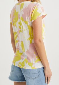 Krátký rukáv top z měkké bavlny, s barevným abstraktním květinovým vzorem v růžové a žluté na bílém pozadí.