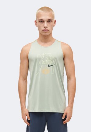 Jeune homme aux cheveux blonds courts portant un débardeur vert clair Nike et un short bleu marine, regardant de face avec une expression neutre.