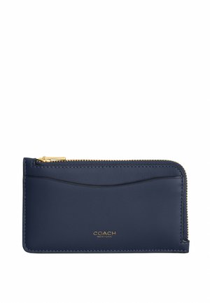 Porte-cartes en cuir bleu marine avec fermeture éclair dorée sur le dessus, emplacement externe incurvé pour cartes, et petit logo COACH New York doré centré en dessous.