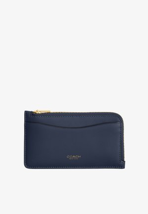Porte-cartes en cuir bleu marine avec fermeture éclair dorée sur le dessus, emplacement externe incurvé pour cartes, et petit logo COACH New York doré centré en dessous.