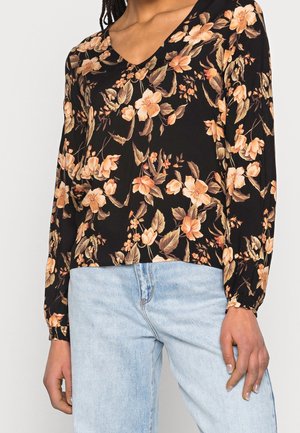Blusa nera a maniche lunghe con motivo floreale in tonalità di pesca e crema, dotata di scollatura a V e polsini arricciati. Abbinata a un jeans denim blu chiaro.