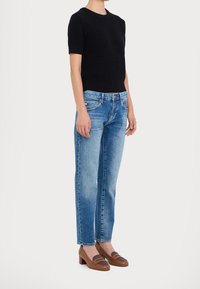 Haut noir à manches courtes côtelé associé à un jean droit bleu clair et des mocassins marron avec des accents texturés et un talon moyen.