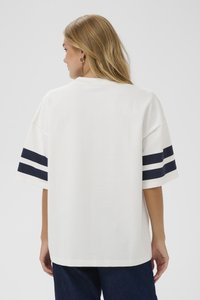 Biele oversized tričko s námorníckymi modrými pruhmi na rukávoch. Má uvoľnený strih a jemnú textúru látky. Zobrazený je pohľad zozadu.