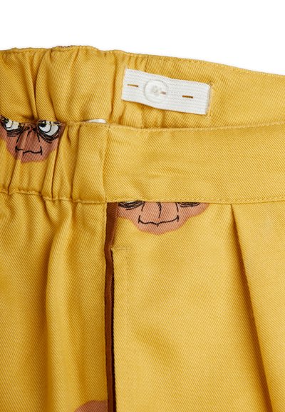 Κίτρινη ελαστική ζώνη με ρυθμιζόμενη λευκή κουμπότρυπα και εκτυπωμένα πρόσωπα καρτούν που είναι μερικώς ορατά κάτω από το ύφασμα.