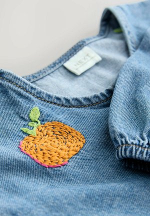 Haut en denim avec un col rond, présentant une broderie de fruit orange, une feuille verte et un accent rose, avec des manches élastiques et des coutures bleues.