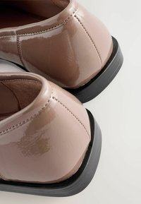 Glänzendes beiges Schuhwerk mit runder Zehenpartie und schwarzer Gummisohle. Verfügt über gestickte Akzente und eine glatte, strukturierte Oberfläche.