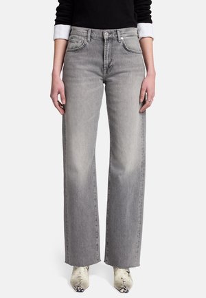 Osoba nosząca szare, szerokie dżinsy z wysokim stanem i czarną bluzkę z długim rękawem oraz białe mankiety, połączone z białymi, szpiczastymi butami ze skóry węża.