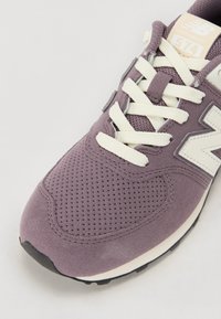 Lilla semsket sneaker med meshnets, med kremfargede snører, en beige tungeetikett og en kontrasterende svart gummisåle.