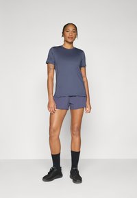 Marine idretts T-skjorte med korte ermer og logo på ermet, kombinert med matchende shorts. Grå teksturerte joggesko og sorte sokker.
