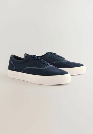 Donkerblauwe canvas sneakers met witte rubberen zolen, ronde neuzen en contrasterende witte stiksels. Inclusief zes veterogen en een gewatteerde kraag.