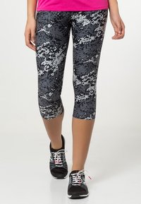 Leggings de patrón negro y gris con un corte a media pantorrilla, hechos de un material elástico, combinados con zapatillas deportivas negras.