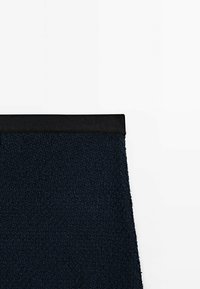 Mörkblå fleeceplagg med en texturerad yta, utrustad med ett svart elastiskt midjeband. Designen är minimalistisk med rena linjer.