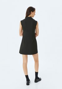 Ärmelloses schwarzes Kleid mit Kragen, tailliertem Design und knielangem Saum. Aus glattem Stoff gefertigt, mit Nahtdetails und minimalistischem Stil.