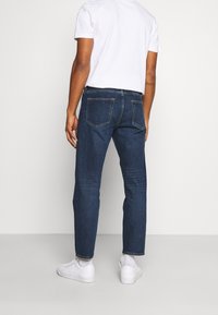 Tmavě modré džíny s rovný fit, mají dvě zadní kapsy a mírné vyblednutí. Spárované s bílým tričkem a teniskami.