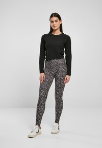 Maglia nera a maniche lunghe abbinata a leggings neri e bianchi con motivi astratti, completata da sneaker bianche con dettagli verdi.