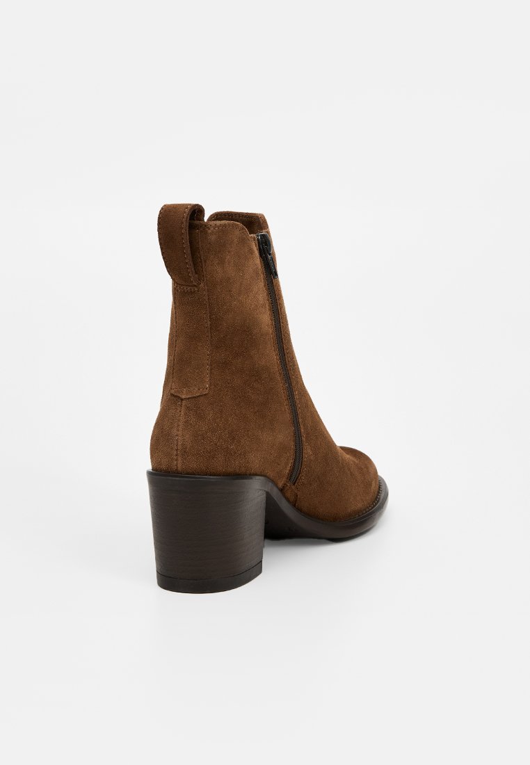 Bottine en daim brun avec un petit talon bloc, fermeture éclair sur le côté et languette de traction. La texture est douce et le design présente une silhouette ajustée.