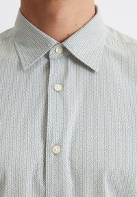 Hellblaues Hemd mit einem Fischgrätenmuster, ausgestattet mit einem Button-Down-Kragen und weißen Knöpfen. Der Stoff hat eine glatte Textur.