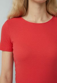 Czerwona, prążkowana koszulka z okrągłym dekoltem i krótkimi rękawami, wykonana z elastycznego materiału, podkreślająca dopasowany krój.