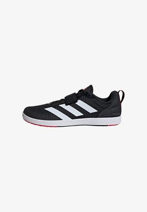 Zapatilla deportiva negra con parte superior de tejido texturizado, presenta tres rayas blancas, correa de Velcro y una suela distintiva blanca y roja.
