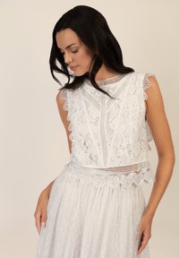 Hvid blonde top med bølgede kanter og indviklede blomster mønstre, parret med en gennemsigtig hvid nederdel med prikker.