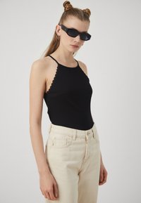 Black ribbed halter top with scalloped edges, paired with high-waisted beige jeans. Accessories include sleek black sunglasses.