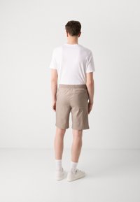 Beige shorts med elastisk talje, sidelommer og en glat tekstur, parret med en hvid t-shirt og hvide sneakers.