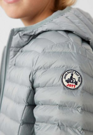 Bambino che indossa una giacca imbottita grigio chiaro con cappuccio, che mostra una toppa rotonda sulla spalla con uno scooter e la scritta "Just over The Top JOTT."