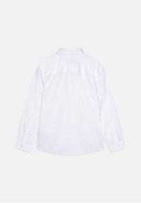 Chemise blanche à manches longues, posée à plat et montrant le dos, avec des poignets boutonnés et un col standard sur un fond blanc uni.
