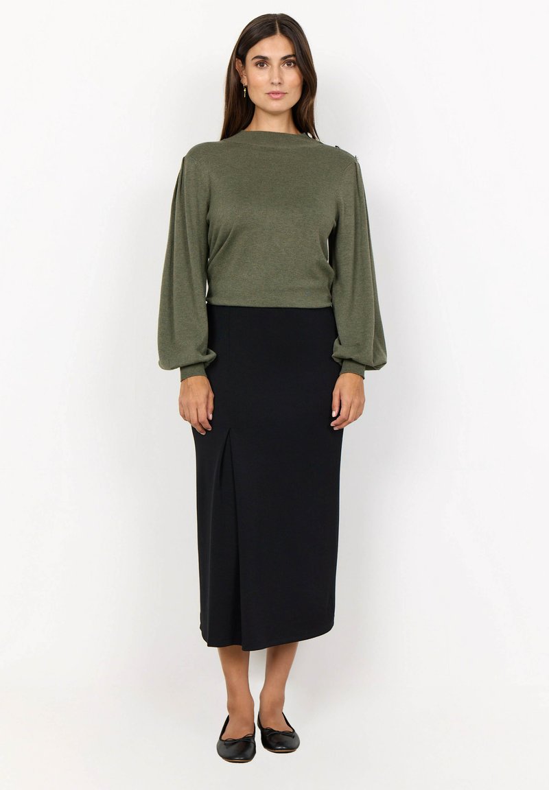 Olivgrünes Langarmoberteil mit Ballonärmeln, kombiniert mit einem taillierten schwarzen Midirock mit seitlichem Schlitz. Schwarze Ballerinas runden das Outfit ab.