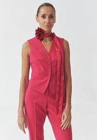 Fuksija odijelo s prslukom i hlačama s gumbima, koje dolazi s odgovarajućim satin maramom i cvjetnim akcentom, ističe elegantnu siluetu.