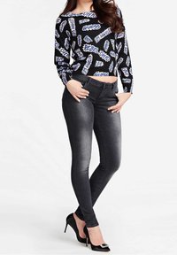 Haut court noir avec texte graphique blanc et bleu, associé à un jean gris foncé ajusté. Des talons hauts noirs avec un accent orné de bijoux complètent le look.