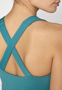 Teal Sport Tanktop mit gekreuzten Rückenriemen. Hergestellt aus glattem Stoff, mit enganliegendem Schnitt und sauberer Naht entlang des Halsauschnitts.