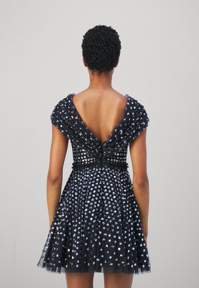 Rochie din tul negru cu corset ajustat, mâneci scurte și un decolteu adânc în spate. Prezintă un model cu puncte argintii răspândite și o fustă evazată.